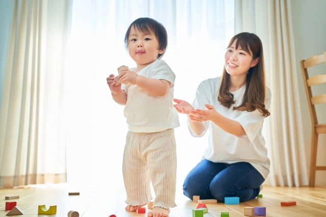 積み木を持って遊ぶ子どもと、笑顔で寄り添う母親